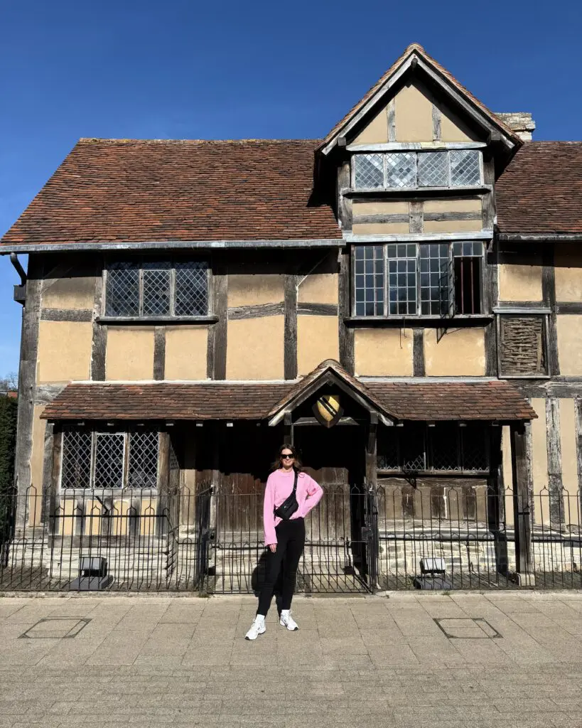 A woman in a pink sweater standing in front of an old, timber framed building