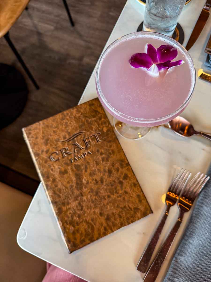 A pink cocktail glass on a table with a brown menu next to it that reads "craft Tampa"