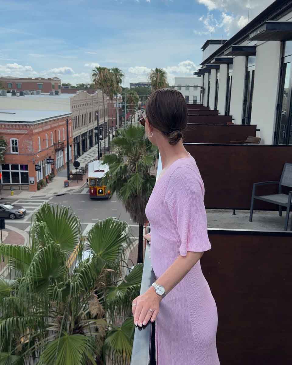Amy in a pink dress looking out from a balcony onto the historic district below where a street car is on the street