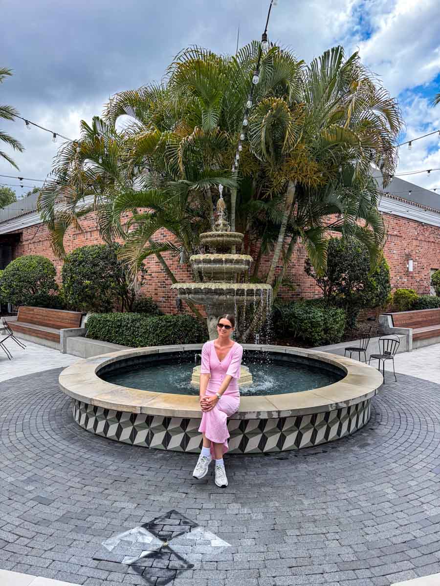 Amy sitting on the edge of a fountain in an outdoor terrace area with a large palm treet behind her