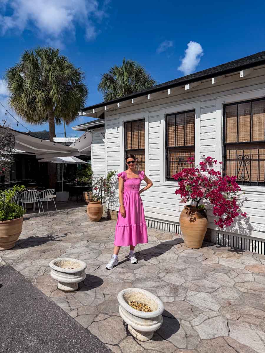 Amy in a pink dress outside a white wooden board building that's Spanish style