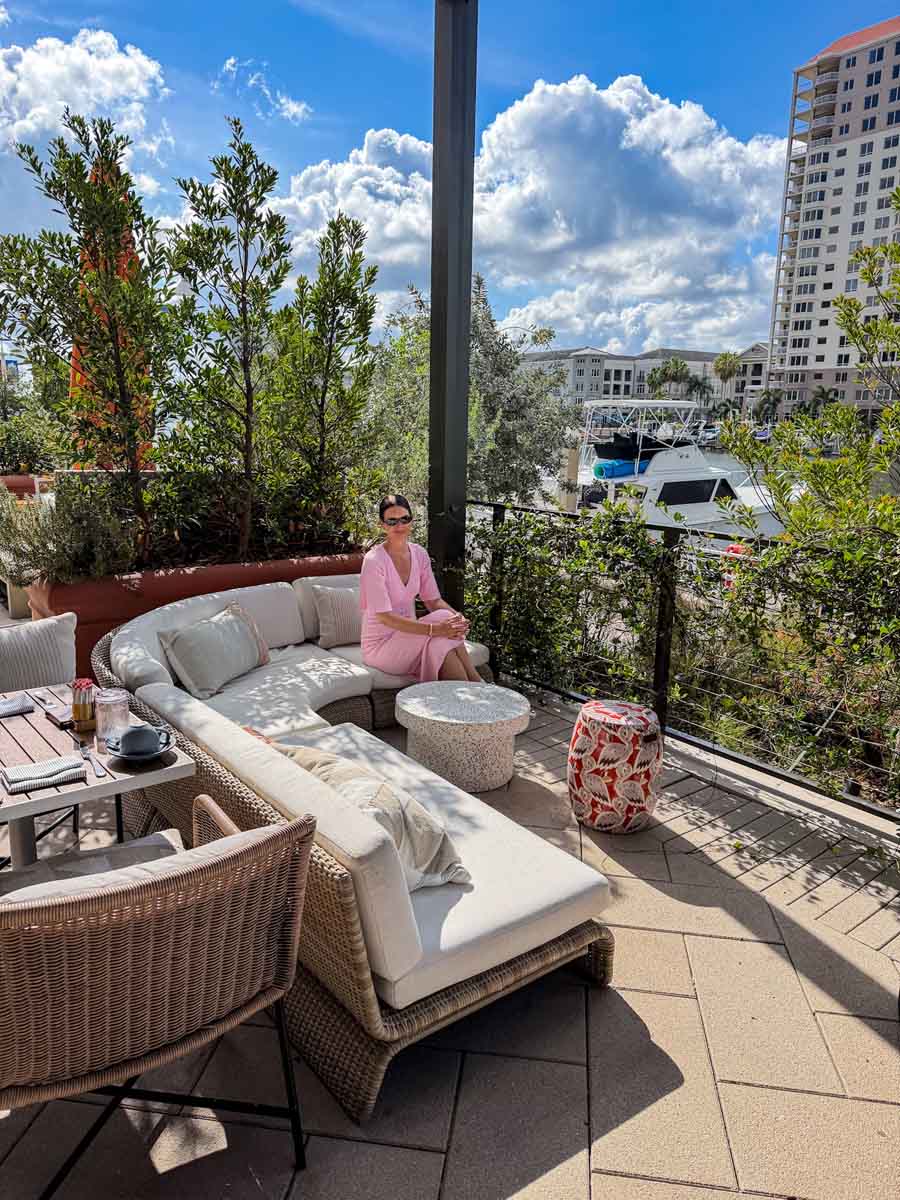 Amy in a pale pink dress on an outdoor sofa on a terrace overlooking the Tampa Bay river on a sunny day