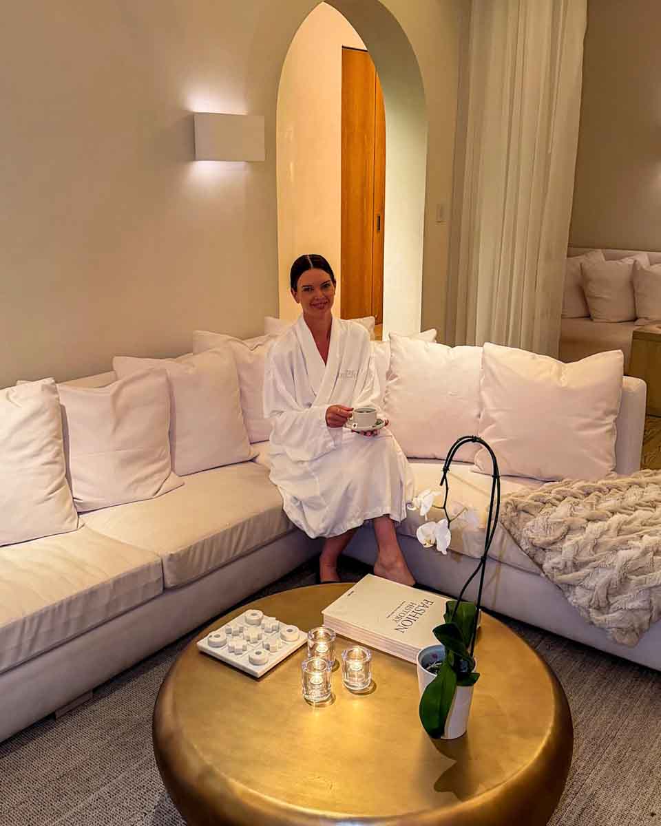 Amy in a white robe sitting on a white sofa in Tampa EDITION spa