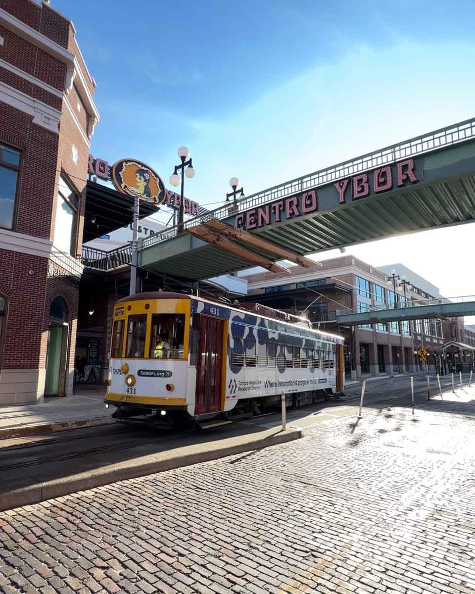 A street car on the tracks, passing under a bridge that reads "Centro Ybor"