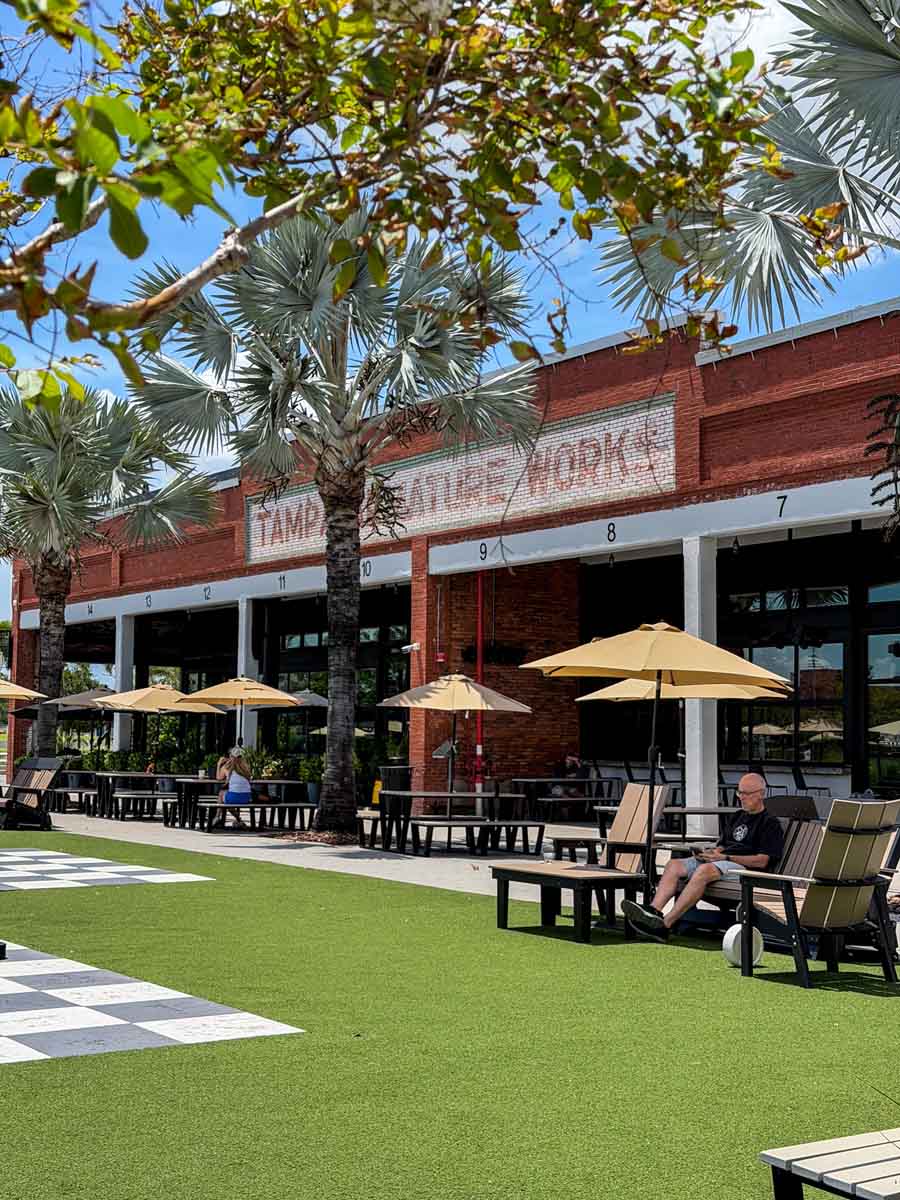 an outdoor eating and seating area in front of an old brick building with palm trees obscuring the front