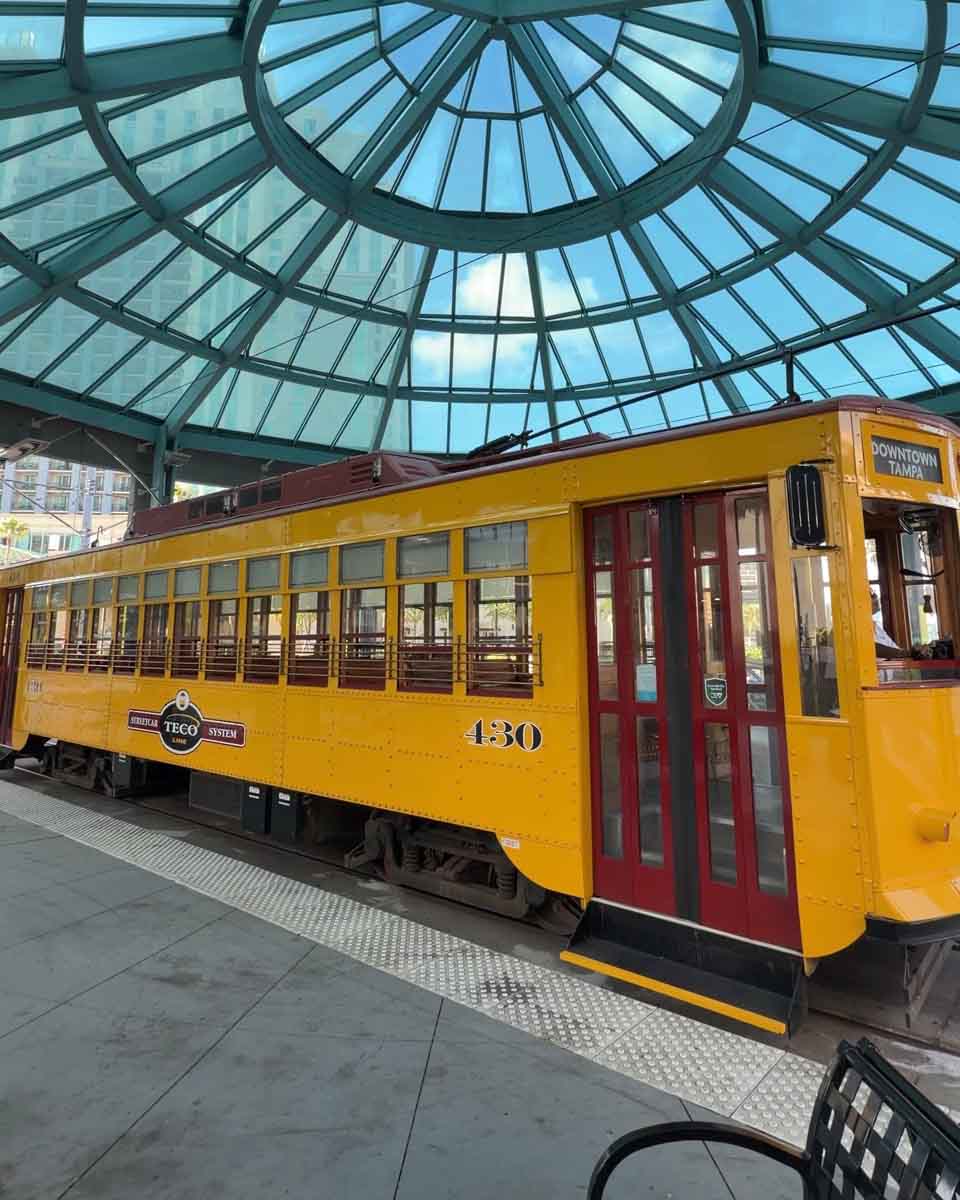 A old fashioned style yellow street car on tracks, underneath a domed glass roof