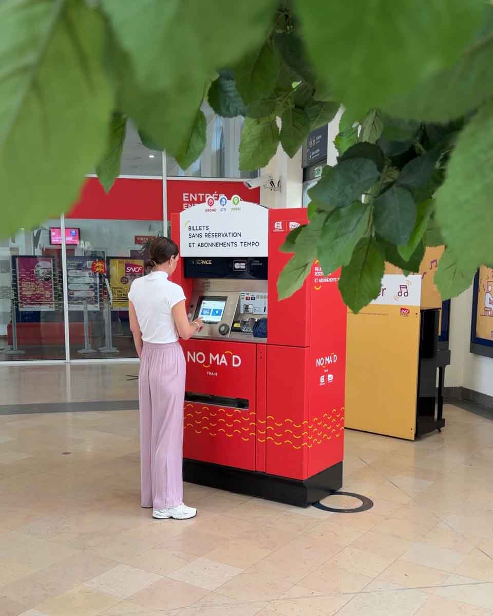 Amy at a ticket machine, buying a train ticket for the NOMAD train to Normandy from Paris