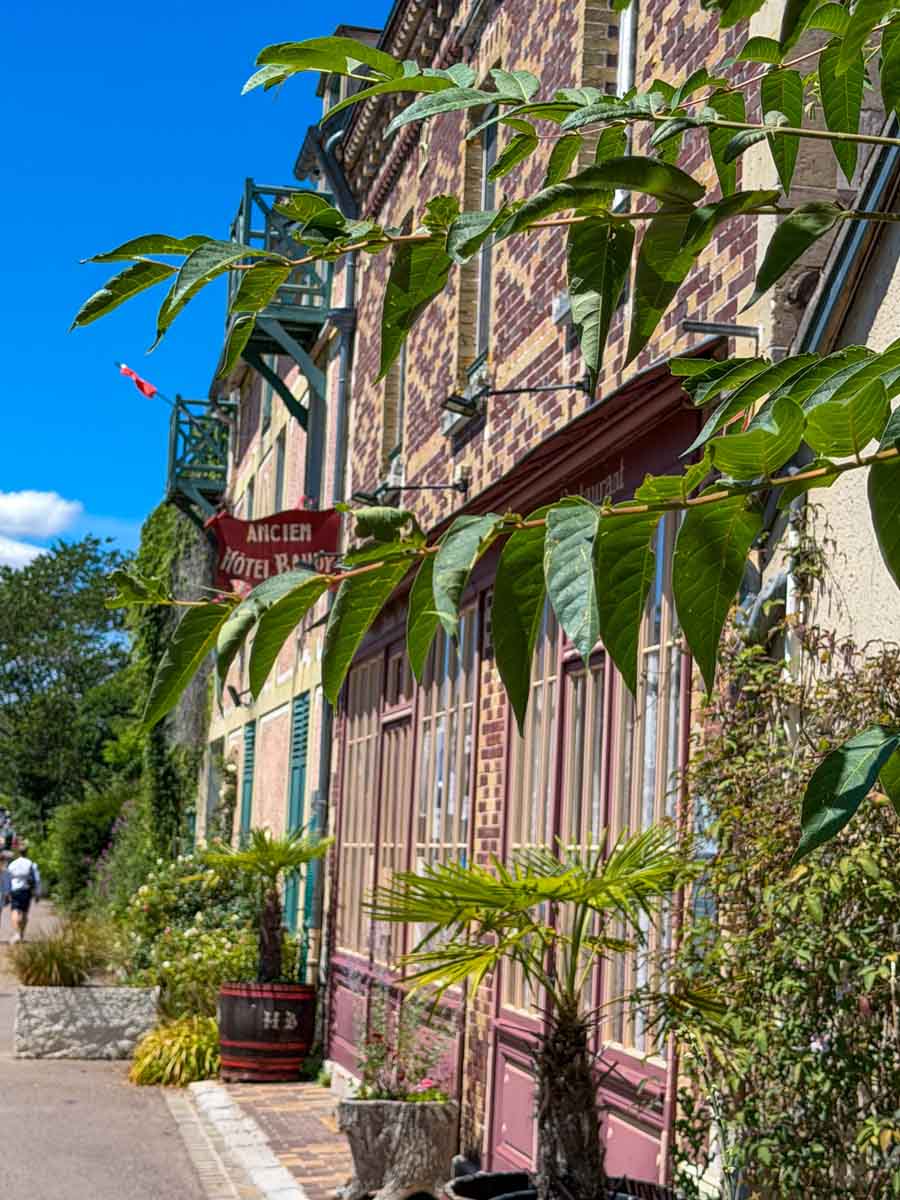 A picturesque street of colourful green and red brick houses covered in greenery with blue sky beyond
